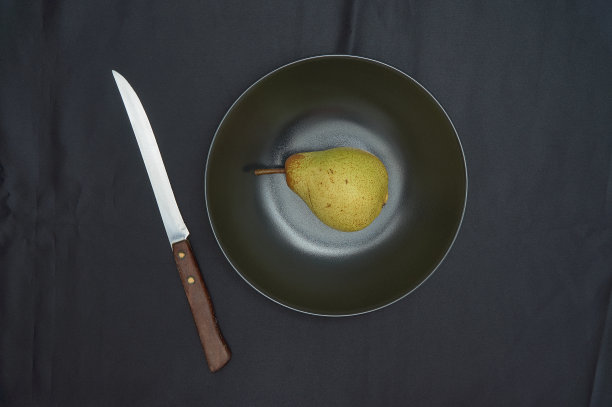 黑色盘子上的绿梨和黑色背景上的刀的静物。图片下载