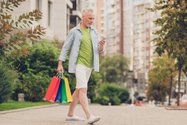 照片积极放松的成熟男子穿着牛仔裤衬衫走路发短信现代小玩意拿着购物袋城外的城市街道图片下载