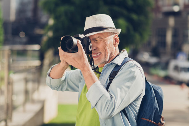 照片自信有吸引力的年龄男孩穿牛仔衬衫帽子背包看照片相机户外街道城市城市图片下载