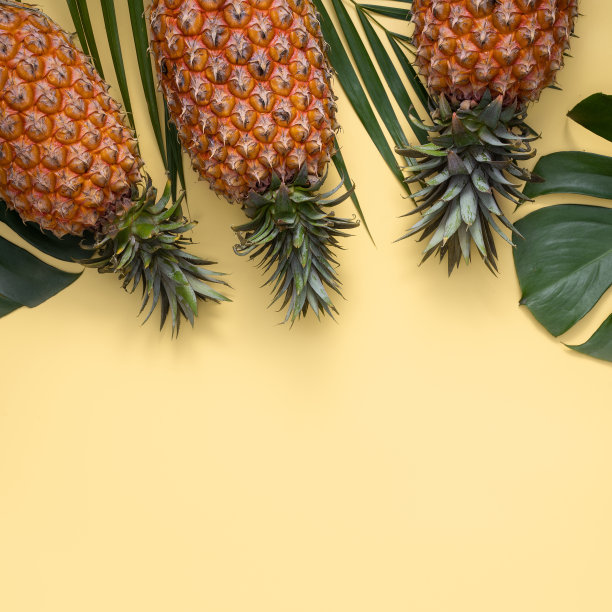 俯视图的新鲜菠萝与热带树叶在黄色的背景。图片下载