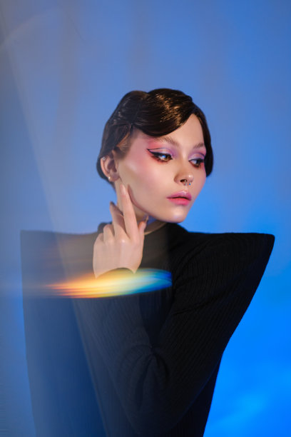 一个年轻漂亮的女模特在工作室里摆姿势。蓝色的光，反射在一个灵活的镜子，玻璃和灯光图案的背景。图片下载