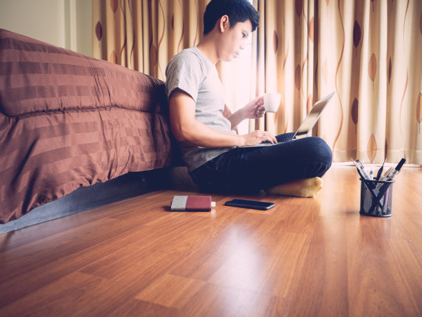 在家工作(WFH)概念。一名男子坐在卧室地板上用笔记本电脑工作。图片下载