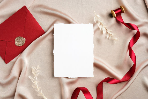 优雅的婚礼文具设置俯视图。平铺空白邀请卡模型，红丝带，信封上的米色缎子。图片下载