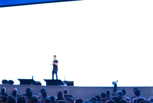 演讲人站在讲台上，面向会议厅或研讨会会场的观众，展示商业和教育理念。在商务会议上发言的演讲者。研讨会演讲的照片。图片下载