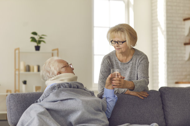 关怀的老伴给一个发烧和喉咙痛的男人一杯水。图片下载