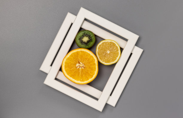灰色背景下的白色矩形。由柠檬，橘子，猕猴桃和白色相框组成的设计构图。图片下载