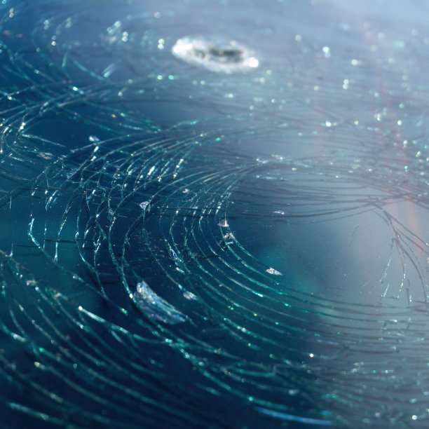 背景蓝色汽车破碎的挡风玻璃上覆盖着圆圈的裂缝。洞在挡风玻璃上。图片下载