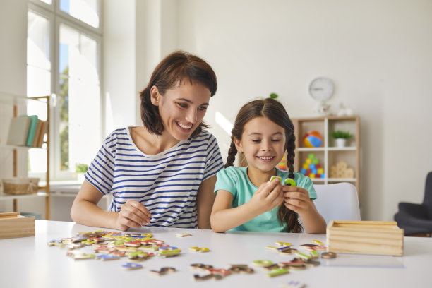 妈妈和小女儿坐在房间里的一张桌子旁拼拼图。图片下载