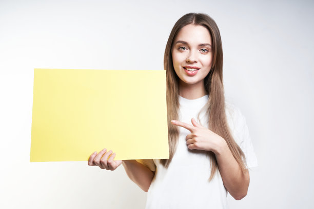 一位身穿白色t恤、灰色背景上举着黄色标牌的金发美女图片下载