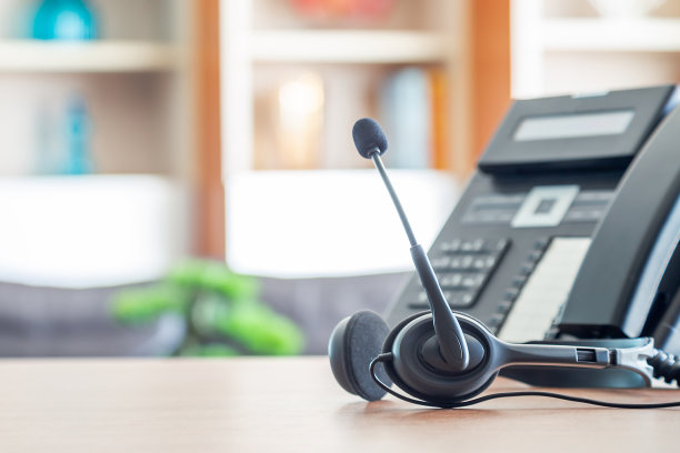 近距离软聚焦耳机与电话设备在办公桌客户服务支持。VOIP耳机用于客户服务支持(呼叫中心)的概念。图片下载