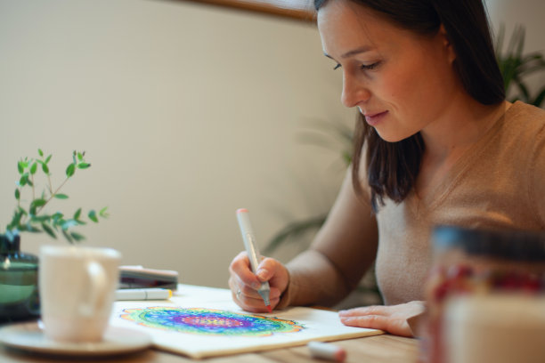 年轻女子用马克笔和白色念珠给曼荼罗上色，桌上放着一杯咖啡图片下载