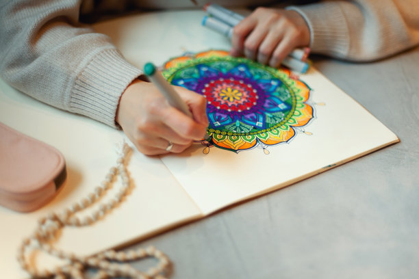 年轻女子用马克笔和白色念珠给曼荼罗上色，桌上放着一杯咖啡图片下载