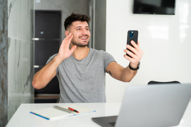 年轻人坐在室内白光明亮的公寓桌子上与朋友通电话。图片下载