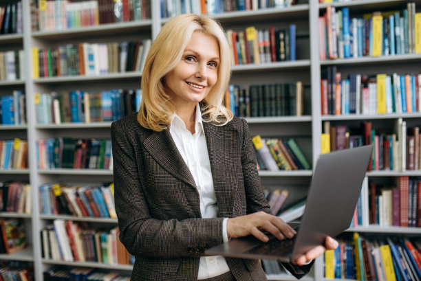 优雅成熟的白人商务女性或教师，穿着正式时尚的套装，拿着并使用笔记本电脑，微笑着直视镜头图片下载