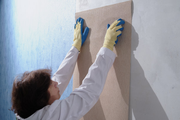在一个普通的城市公寓里，一个穿着白色制服的黑发成人正在把墙纸贴在墙上，这是修缮和施工完成工作过程的最后一个阶段图片下载