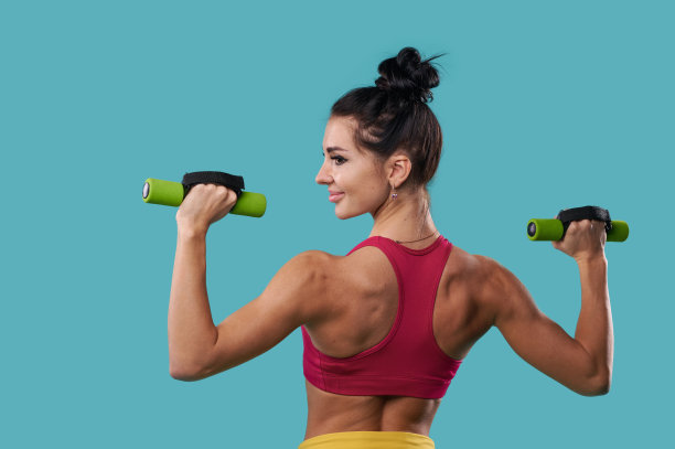 迷人和肌肉发达的年轻女子展示背部肌肉，同时与哑铃图片下载