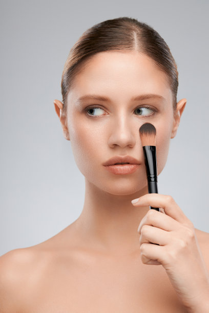 美丽的年轻女士拿着化妆刷和摆姿势在工作室。美摄影图片下载