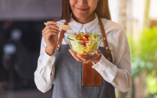 一个年轻漂亮的女厨师拿着和吃着新鲜的混合蔬菜沙拉图片下载