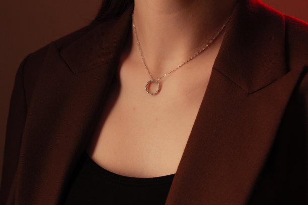 裁剪近距离肖像的年轻女子与完美的丝绸般的皮肤，展示银首饰链与奖章在颈部在棕色夹克图片下载