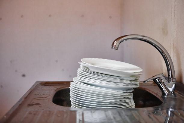 在肮脏的厨房里，水龙头下面的金属水槽里有一大堆脏瓷盘图片下载