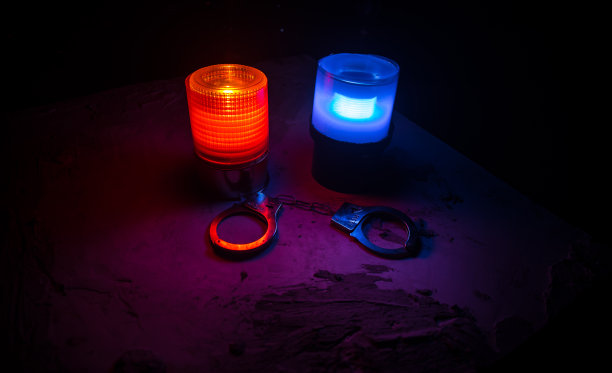 警方夜间突袭，你将被逮捕。手铐的轮廓和警车在后面。在雾蒙蒙的背景下，红色和蓝色警灯闪烁。图片下载