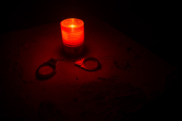 警方夜间突袭，你将被逮捕。手铐的轮廓和警车在后面。在雾蒙蒙的背景下，红色和蓝色警灯闪烁。图片下载