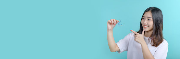 在蓝屏背景上微笑的亚洲妇女持有正畸固位器。牙齿护理和牙齿健康。图片下载