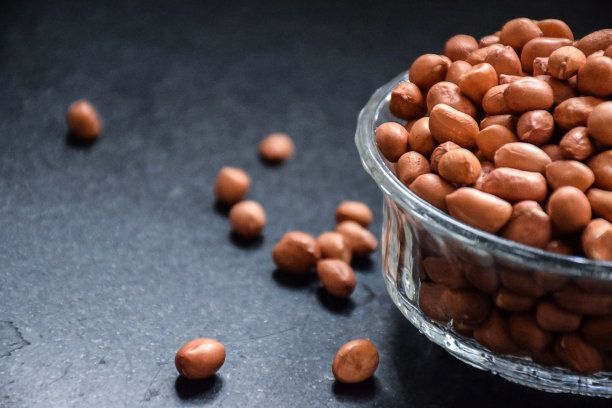 这是一张棕色的生花生放在透明的玻璃碗里的照片，在厨房的自然光下放在黑色的花岗岩上。关注对象。图片下载