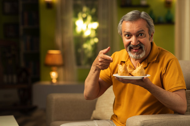 一个成熟的男人在家里吃萨莫萨:库存照片图片下载