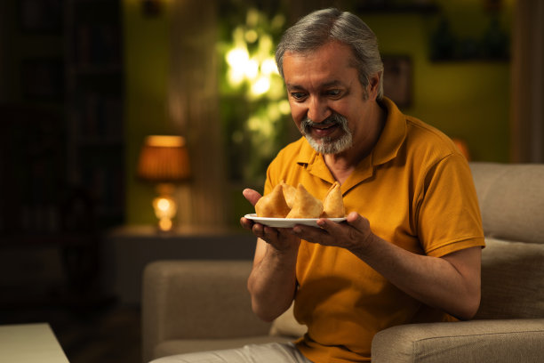 一个成熟的男人在家里吃萨莫萨:库存照片图片下载