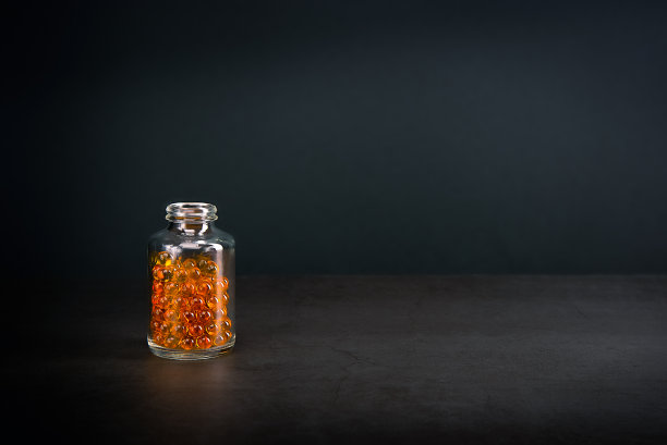 一个在灰色背景上有亮橙黄色药丸的玻璃罐。图片下载