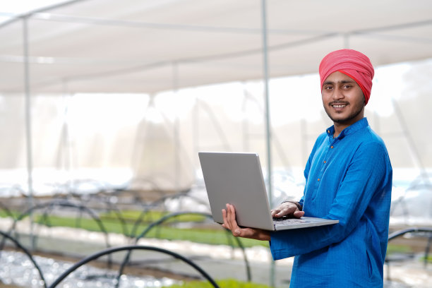 年轻的印度农民在温室或poly房子里使用笔记本电脑图片下载