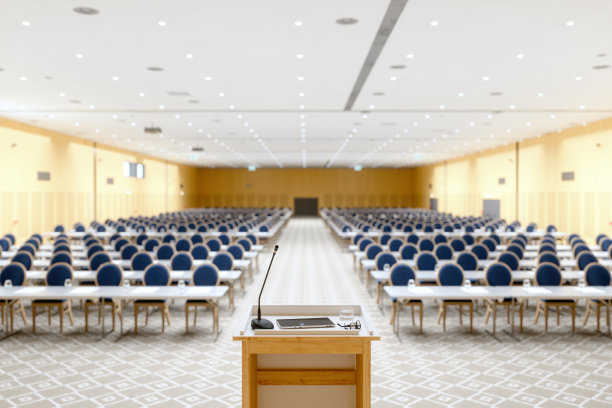 一个空的会议厅的内部。模糊的桌椅背景下的讲台上的麦克风和笔记本电脑。图片下载