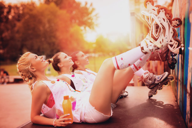 三个漂亮的年轻女孩带着滚轴在滑板公园休息和大笑。图片下载