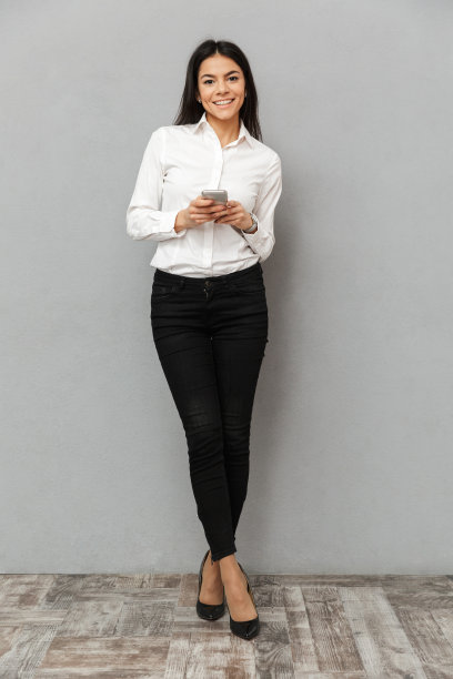 完整的形象，漂亮的商务女性穿着正式，微笑着拿着手机，在灰色的背景孤立图片下载
