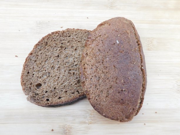 阳光下厨房里刚烤好的两片麦麸面包，上面裹着一层黑麦粉，放在棕色的木桌上图片下载