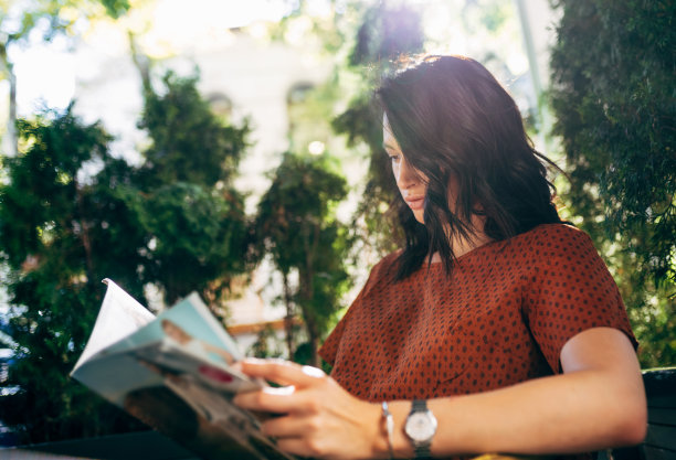 水平的照片，一个快乐的年轻漂亮的女人等待他的朋友在自助餐厅的露台和阅读的书。坐在自助餐厅里的小企业女性高管。图片下载