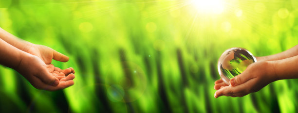 环境概念世界地球日旗帜。双手捧着玻璃绿色星球在阳光灿烂的背景。保存自然。图片下载