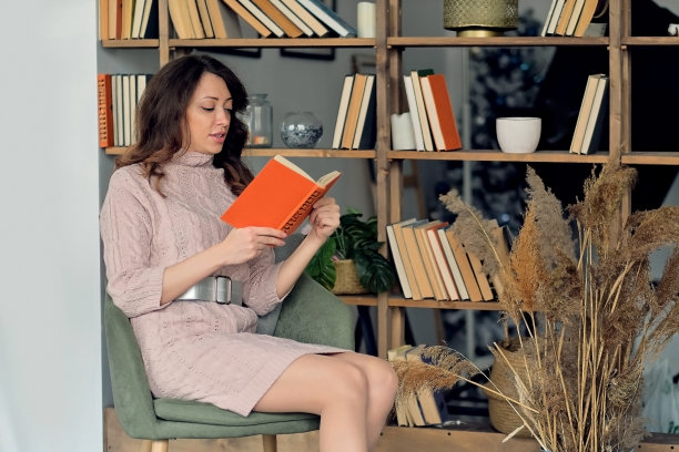 穿着针织连衣裙的年轻现代妇女坐在扶手椅上看书图片下载