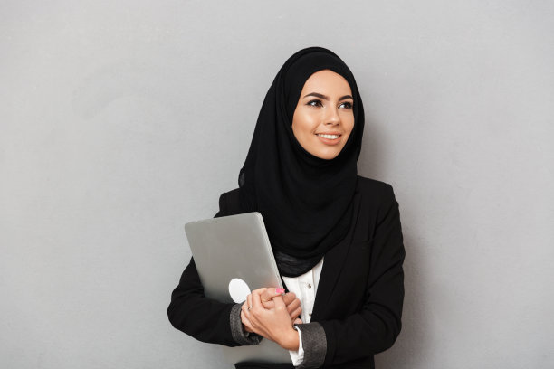 戴黑色传统头巾的阿拉伯微笑妇女肖像，拿着笔记本，灰色背景图片下载
