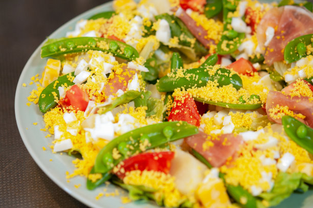 含羞草沙拉与鸡蛋，青豆，西红柿，奶酪和熏火腿放在一个盘子里。充满活力的颜色。特写图片。图片下载