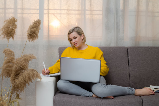 白种女人坐在沙发客厅远程在线工作。2021年的颜色图片下载