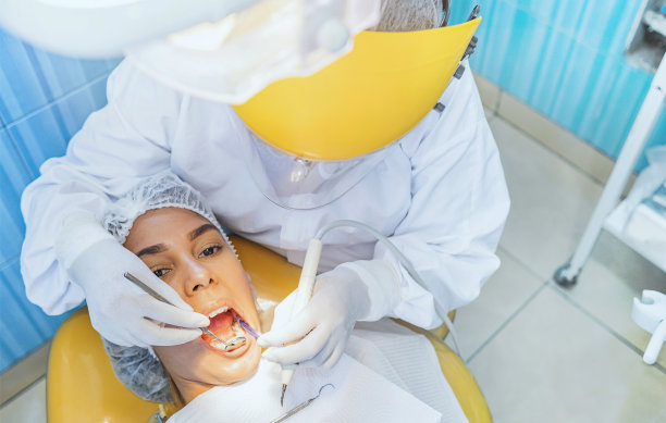 可爱的女人坐在牙医的椅子上，而牙医检查她的牙齿。有选择性的重点。图片下载