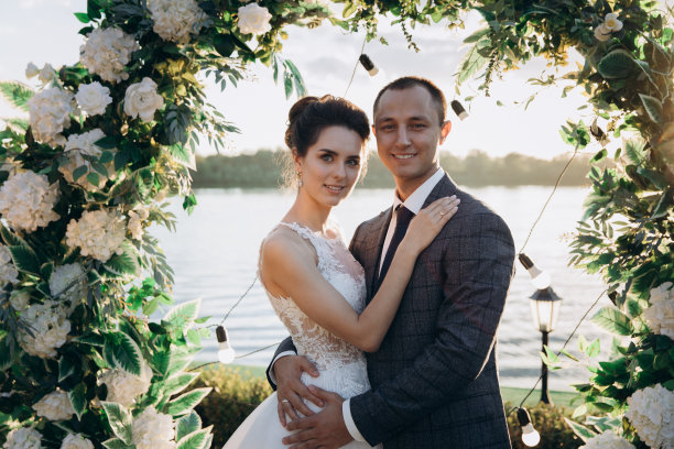 一男一女穿着婚纱在花拱下拥抱。图片下载