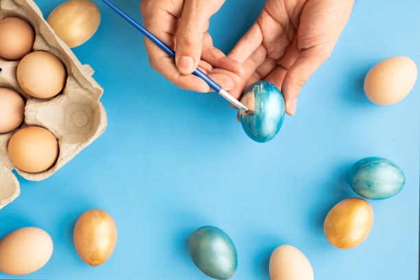 准备复活节。父亲在蓝色的背景上画复活节彩蛋。复活节。图片下载