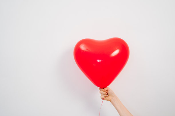 白色墙壁上，一个心形的红色气球。图片下载