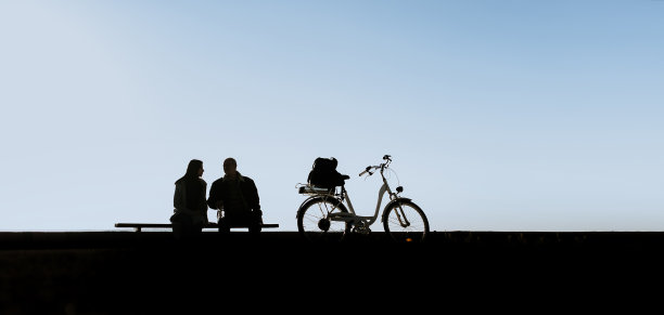 父亲和女儿坐在长凳上聊天。老人和电动自行车。傍晚在河边散步。傍晚在河边散步。图片下载