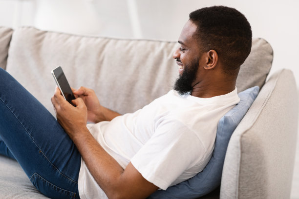 一名非洲男子躺在沙发上使用智能手机图片下载
