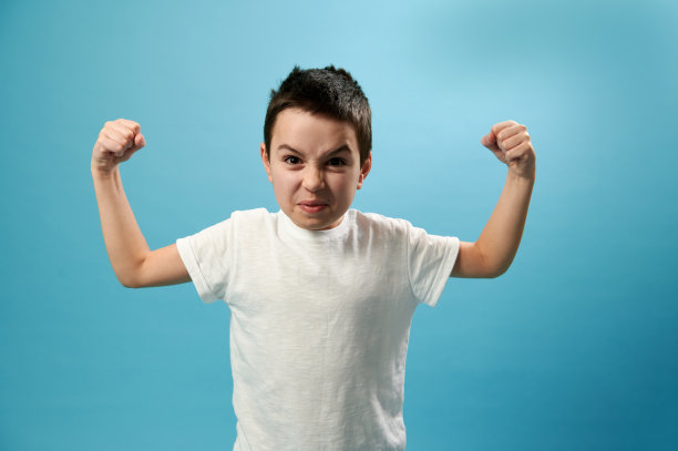 男生泵二头肌和看着愤怒的相机在蓝色背景与复制空间图片下载