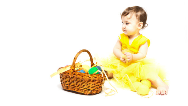 复活节快乐!一个可爱的9个月大的白人小女孩的肖像，穿着一件黄色的小鸡装，在白色的背景和复制空间上，拿着一个装满复活节彩蛋的篮子。图片下载